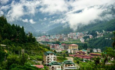 white and brown concrete houses near green trees under white clouds during daytime